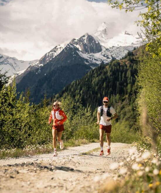 Zwei Trailrunner auf einem Schotterweg im Herbst mti dem verschneiten Kitzsteinhorn im Hintergrund